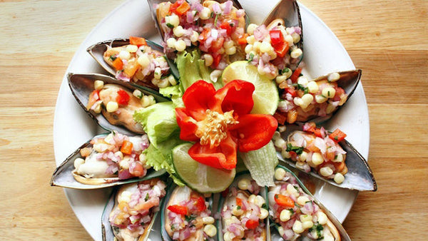 Peruvian mussels topped with Salsa Criolla, showcasing vibrant colors of tomatoes, onions, and a splash of lime.