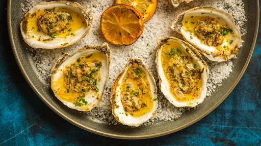 Smoky grilled oysters topped with sizzling chorizo butter and fresh herbs on a rustic serving platter.