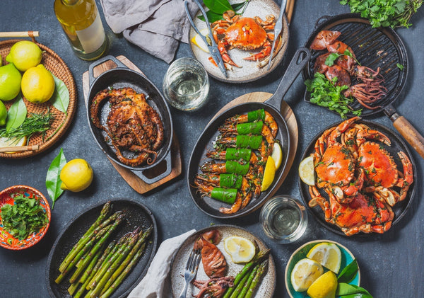 Grilled seafood dishes with fresh lemon, cilantro, and olive oil placed on a black table. 
