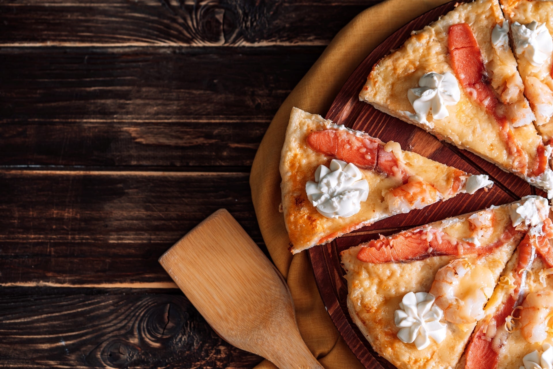Sliced lobster pie topped with chunks of lobster meat and dollops of cream, served on a wooden board over a rustic table.