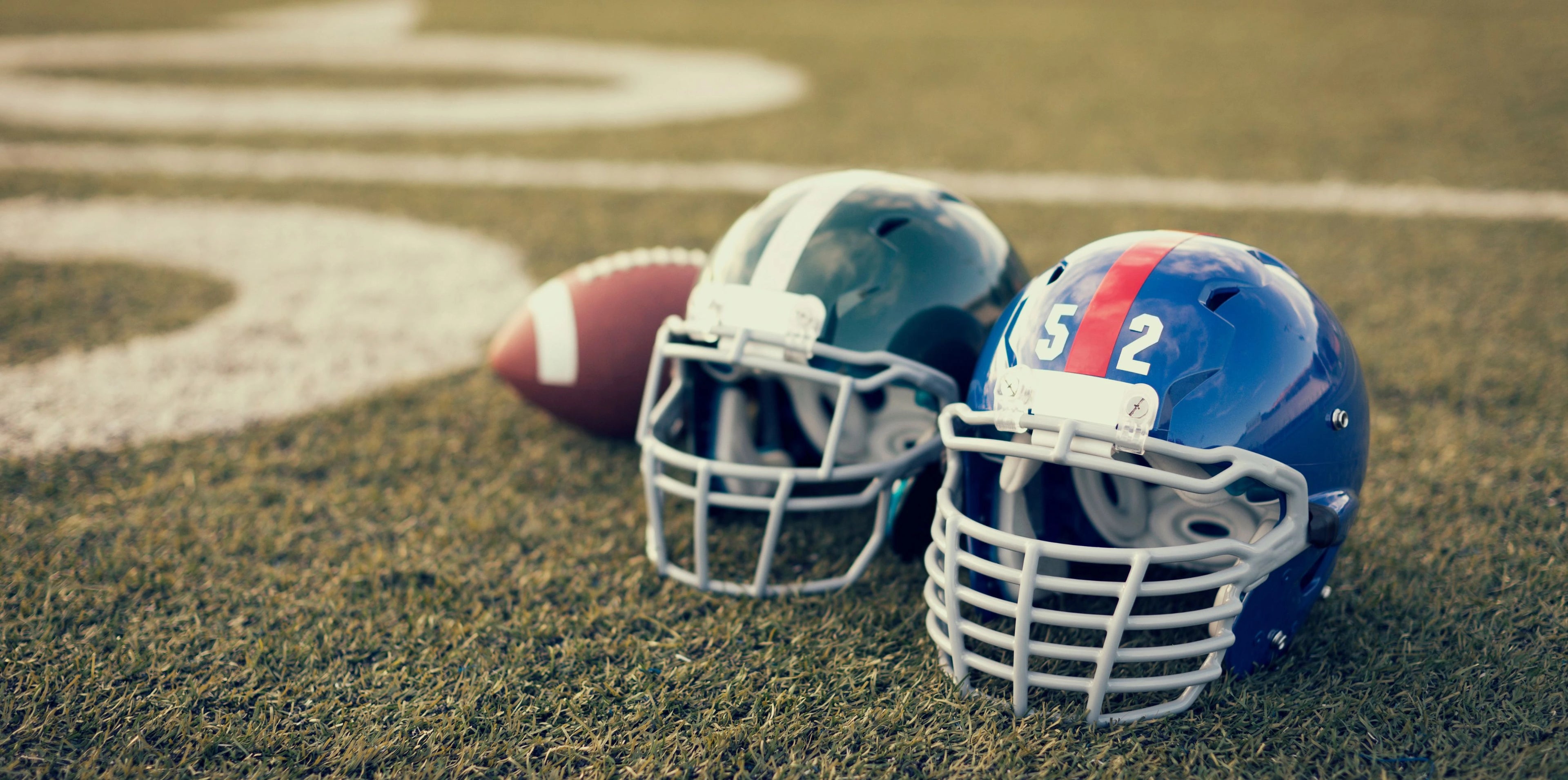 two football helmets and a football laid down on the field