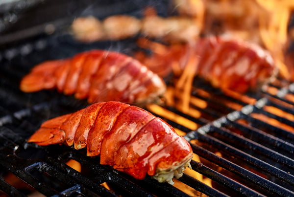 Juicy lobster tails grilling over open flames on a barbecue, showcasing their rich red shells and smoky glaze.