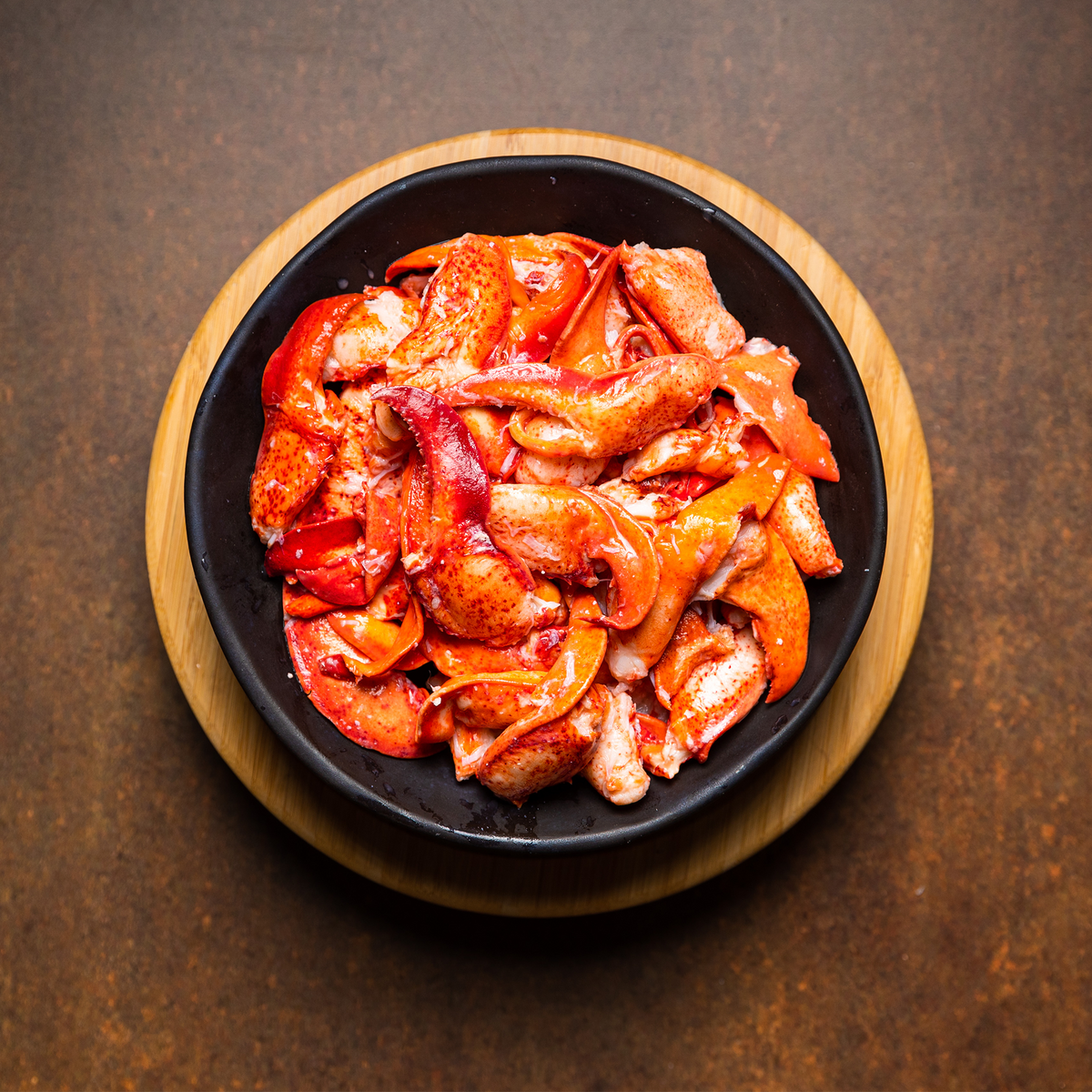 Freshly cooked lobster meat, including claw and knuckle pieces, served in a black bowl on a wooden board—perfect for lobster rolls, salads, or gourmet seafood dishes.