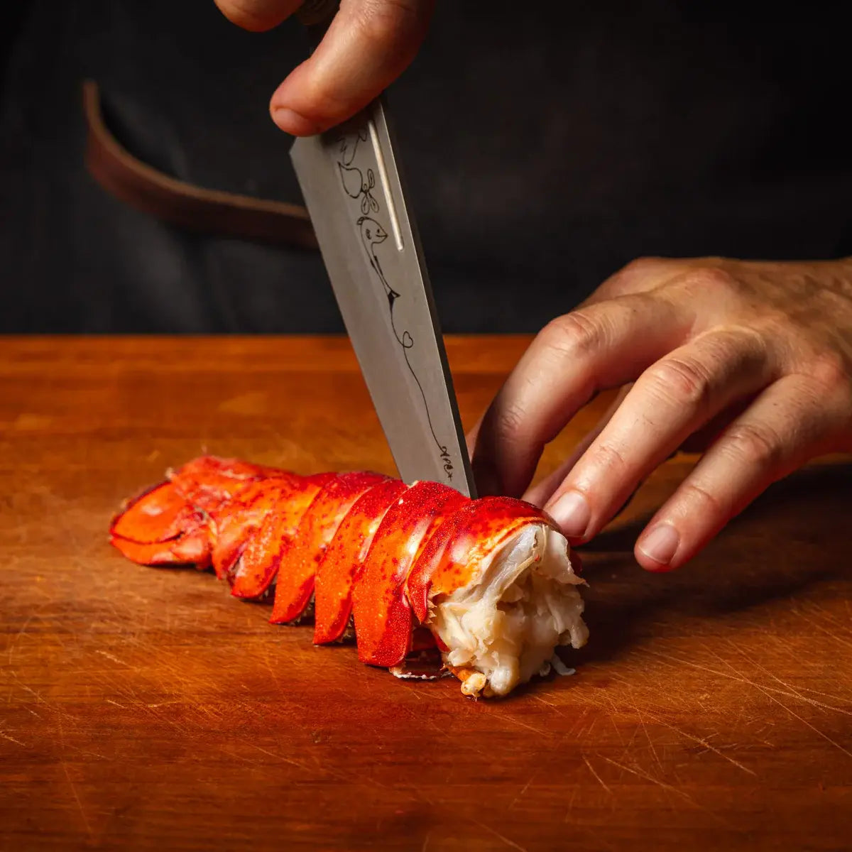 Slicing into a cooked Maine lobster tail on a wooden board.