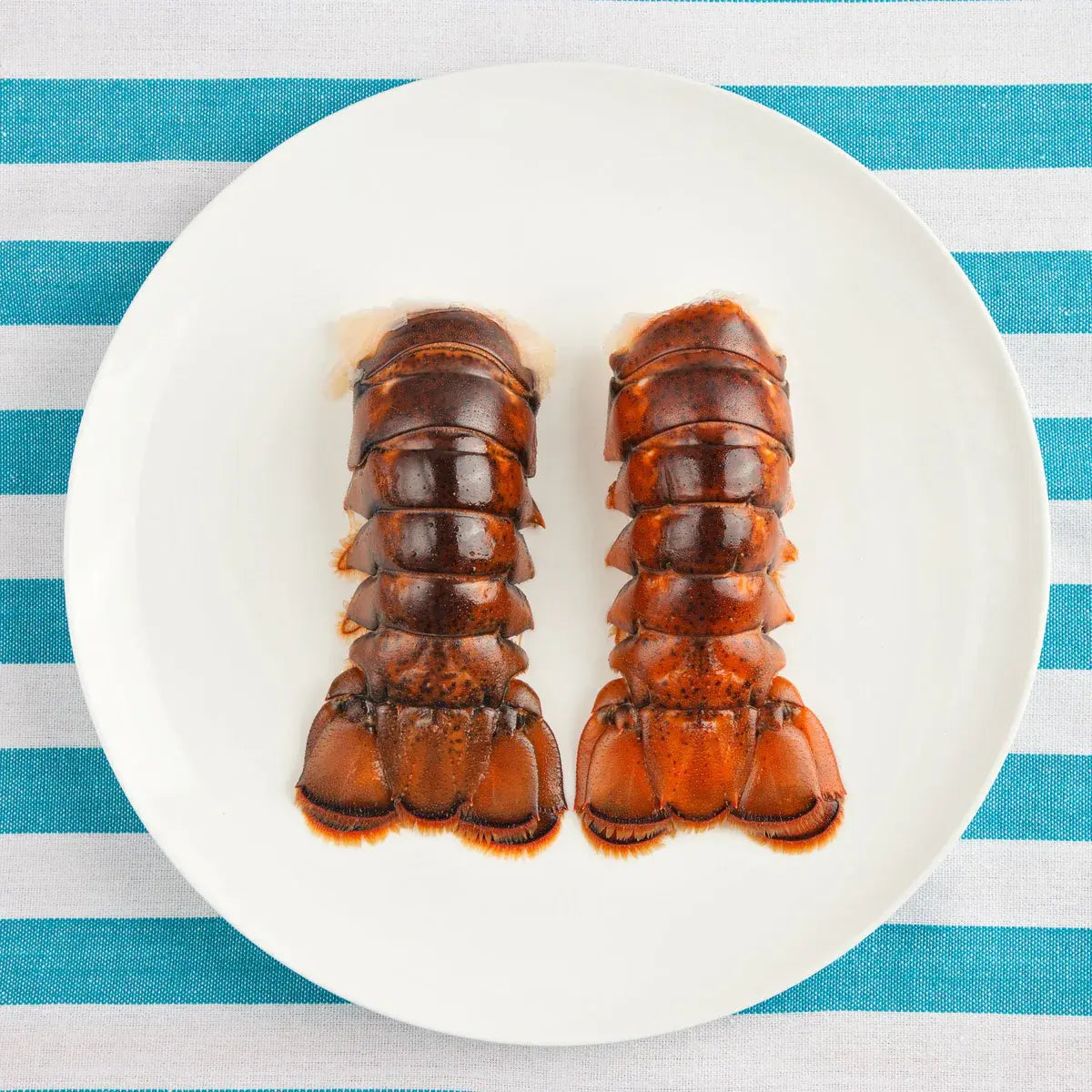 Two raw Maine lobster tails on a white plate, ready for preparation.